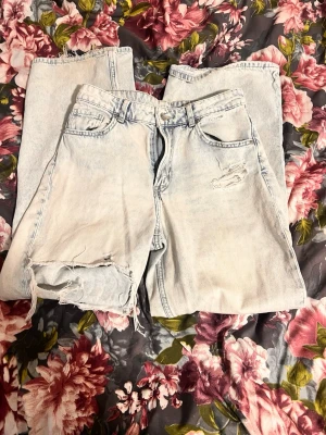 Ljusa ripped jeans  - Säljer ett par ljusa jeans med slitningar och hål vid knät för en cool, avslappnad vibe. Byxorna har klassisk femficksdesign och är tillverkade i jeansmaterial. Perfekt för dig som gillar en edgy och trendig stil.