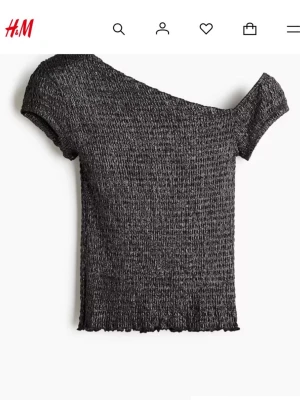 Glittrig svart offshoulder topp H&M - ALDRIG ANVÖND LAPP KVAR.                         Säljer en svart glittrig topp från H&M med offshoulder-design och korta ärmar. Toppen är croppad och har en smockad, stretchig struktur.