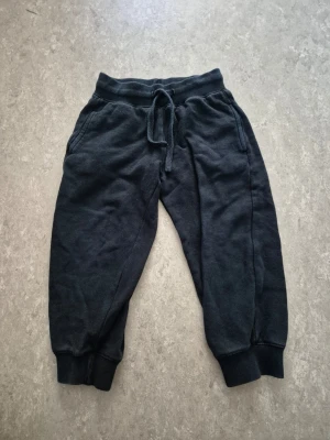 Mjukisbyxor - Svarta mjukisbyxor från Basic U med ribbade muddar vid benslut och midja. Byxorna har snörning i midjan och två sidofickor. Tillverkade i mjukt bomullsmaterial, perfekta för chill och häng. Passformen är loose och färgen är mörk svart. Finns några hål.