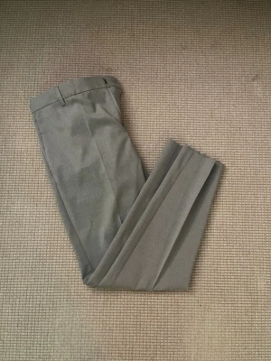Grå skinny kostymbyxor från H&M - Slimmade grå kostymbyxor från H&M i storlek 34. Byxorna har skinny fit, pressveck och bälteshällor. Materialet är mjukt och har en lätt struktur som ger en clean och modern look. Perfekt för dig som gillar stilrena och smala siluetter.