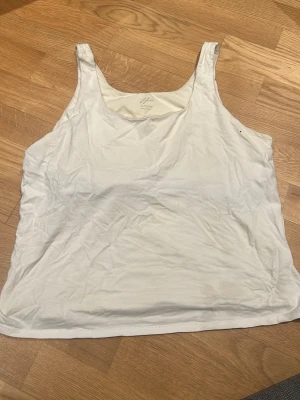 Vit linnetopp från J.Jill - Säljer en vit linnetopp från J.Jill med inbyggd shelf-bh. Toppen är ärmlös och har breda axelband. Materialet är mjuk bomull med lite stretch tack vare lycra och spandex. Perfekt för varma dagar och enkel att matcha med andra plagg.