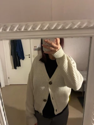 Beige stickad kofta från Vero Moda - Säljer en beige stickad kofta från Vero Moda med grov ribbad struktur och tre stora bruna knappar framtill. Koftan har v-ringad hals och lång ärm.