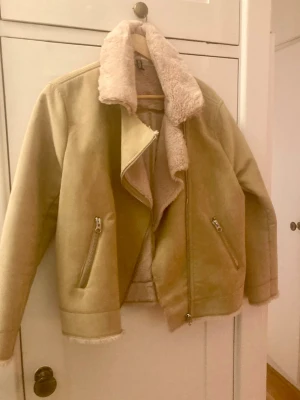 Beige teddyjacka med dragkedja - Säljer en beige teddyjacka från H&M med mjuk fuskpäls på kragen och insidan. Jackan har två fickor med dragkedja och en sned dragkedja framtill. Perfekt för dig som gillar mysiga och trendiga jackor med lite oversized känsla.