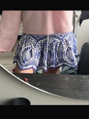 Blåvit kortkjol med mönster - Superfin kort kjol från ZARA med blått orientaliskt/bohemiskt mönster och volangig nederdel. Dekorknappar med pärlliknande look framtill som ger en söt och unik detalj. Den är väldigt högmidjad. Knappt använd, jättefint skick. Finns inga oönskade skador, hål eller fläckar. Tyvärr är den nerpackad, därav kan jag inte leta upp vilken storlek den har men det är antingen XS eller S