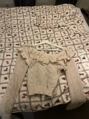 Beige stickad u ringad tröja med volang - Säljer en beige stickad tröja med lång ärm och bred volang i spets runt halsen från Zara som inte säljs längre.  Tröjan har ett snyggt mönster och u ringad design. Andväns endast 1 gång