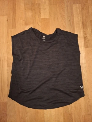 Svart träningströja från SOC - Säljer en svart träningströja från SOC i storlek XS. Toppen har en rund halsringning och är tillverkad i ett lätt syntetmaterial med diskret melerad effekt. Perfekt för träning eller aktiva dagar. Enkel och stilren design med liten logga nere vid kanten.
