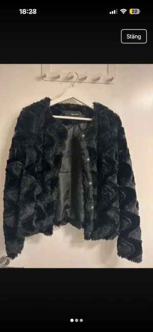 Svart pälsjacka från Vero Moda - Mysig svart pälsjacka från Vero Moda med snyggt vågigt mönster i pälsen. Jackan har knäppning framtill med knappar och är helfodrad. Perfekt för dig som vill ha en statementjacka med cool textur och klassisk look.