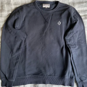 Mörkblå sweatshirt från Morris, S men sitter som S/XS - Mörkblå sweatshirt från Morris med broderad logga på bröstet. Tröjan har rund hals, ribbade muddar och lång ärm. Materialet är mjuk bomull och passformen är normal. Perfekt för dig som gillar stilrena och klassiska plagg med diskreta detaljer.