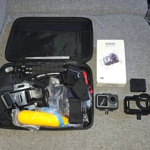 DJI Osmo Action - DJI Osmo Action actionkamera i fint skick, komplett med originalförpackning, batteri, SmallRig-hus och flera tillbehör som handtag, fästen och flytgrepp. Perfekt för äventyr och sport. Inga synliga defekter eller slitage på kameran eller tillbehören. Kameran har dubbla skärmar: en färgstark frontskärm och en pekskärm på baksidan. Den kan spela in 4K HDR-video med 60 bilder per sekund och har RockSteady elektronisk bildstabilisering för jämna bilder.  Den är designad för att vara hållbar och vat