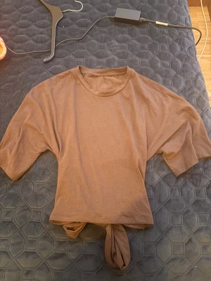 Brun croppad topp med knyt - Säljer en brun croppad topp i mjuk bomull med korta ärmar och rund hals. Toppen har en snygg knytning framtill som ger en chill vibe och gör den extra unik. Perfekt för dig som gillar enkla men coola plagg med twist.
