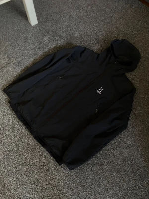 Haglöfs vindjacka - Svart vindjacka från Haglöfs i storlek L. Materialet är lätt och syntetiskt, perfekt för blåsiga dagar. Stilren och enkel design. Rekomenderar verkligen…..