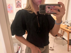 Svart blus med puffärm och knyt - Säljer en svart blus med puffiga korta ärmar och  knytningar framtill. Blusen har blommigt mönster i tyget och en lätt croppad passform. Knappt använd och super fin att ha på ny år❤️