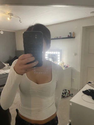 Vit långärmad topp från H&M Divided - Säljer en vit långärmad topp från H&M Divided med snygg v-ringad hals och lätt rynkning vid bysten. Modellen är slim och croppad, perfekt till jeans eller kjol. Materialet är mjuk bomull med lite stretch för skön passform.