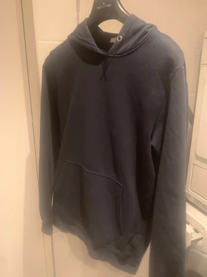 Mörkblå hoodie med huva - Snygg mörkblå hoodie från Batistini med klassisk huva och stor magficka framtill. Tröjan har långa ärmar och en enkel, stilren design som passar perfekt till jeans eller joggers. Materialet är mjukt och skönt, troligen bomull eller polyester.