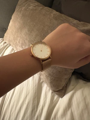 Stilren guldig mesh-klocka - Säljer en elegant klocka med rund urtavla i vitt och guldiga detaljer. Klockan har ett minimalistiskt utseende med guldigt mesh-armband i metall och tunna indexmarkeringar. Perfekt för dig som gillar enkel och snygg design.