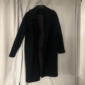 Svart lång kappa från Åhléns , stl 38 - Säljer en svart, stilren och lång kappa från Åhléns i storlek 38.  Nypris 2300kr