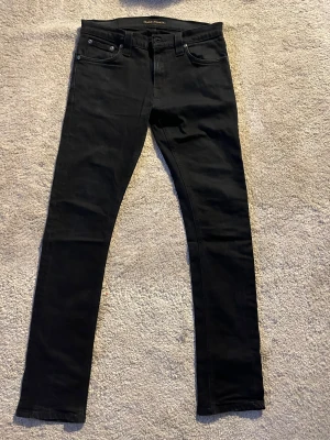 Svarta jeans från Nudie Jeans - Säljer ett par svarta jeans den Nudie i modellen Tube tom. Storleken är 29/32. De är slitna vid skrevet men annars inga defekter. Hör av dig om du undrar något😁