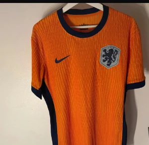 Hollands landslagströja Nike XL orange - Säljer en orange fotbollströja från Nike för Nederländernas landslag. Tröjan har korta ärmar, blå detaljer vid krage och ärmslut, samt KNVB-emblem på bröstet. Tillverkad i Dri-Fit polyester för bästa komfort under matchen.