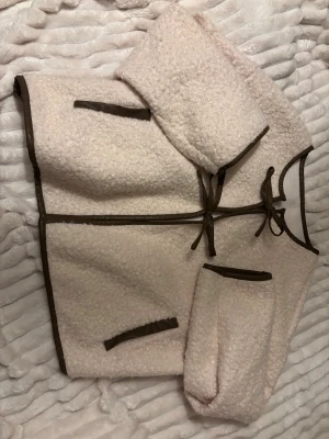 Ljus teddyjacka med bruna detaljer - Säljer en ljus teddyjacka med bruna kantband och snörning framtill. Jackan har två fickor med bruna detaljer och en mysig, fluffig yta. Passar dig som vill ha något mjukt och trendigt. Använd 1 gång ifrån Shein 