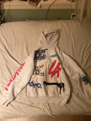 Vit hoodie med graffiti från Black Squad - Säljer en vit hoodie från Black Squad i storlek XS med relaxed fit. Hoodien har färgglada graffiti-prints i rött, blått, svart och gult både fram och bak, samt texten 'Drip2Hard' och 'Worldwide'. Mjuk insida och klassisk huva, perfekt för streetwear-stilen. Den har en fläck på armen 