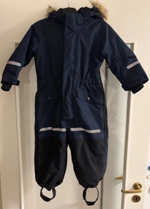 Kaxs Vinteroverall strl 92 - Overallen är i mycket fint skick, förutom att reflexerna har lossnat på vissa ställen.  Banden är hela och ärmarna lika så.  Köpt på Kappahl. 