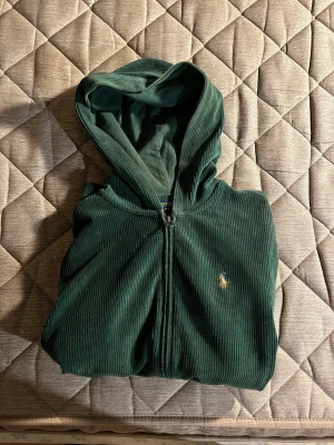 Grön hoodie från Polo Ralph Lauren - Snygg mörkgrön hoodie från Polo Ralph Lauren i mjuk manchester med huva och dragkedja framtill. Tröjan har ribbad struktur, lång ärm och klassisk Polo-broderi på bröstet. Perfekt för dig som gillar chill och stilren look. Kan sänka priset lite vid snabb affär!