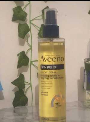 Aveeno Skin Relief Body Oil Spray - Aveeno Skin Relief Body Oil Spray med havreolja och jojobaolja, perfekt för torr och känslig hud. Sprayflaska i transparent plast med blått lock, innehåller 200 ml. Oljan är ljusgul och absorberas snabbt för mjuk och återfuktad hud.