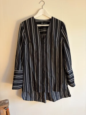 Svart och vit randig overshirt från Lindex - Svart och vit randig overshirt från Lindex i storlek S. Jackan har lång ärm, v-ringad hals och dragkedja framtill med rund ring som zip puller. Materialet är lätt och känns som bomull, perfekt för lager-på-lager. Snygg detalj med olika randmönster på ärmslut och nederkant.