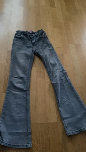 Grå bootcut jeans från D-XEL - Snygga grå jeans från D-XEL i storlek 13/158. Modellen har klassisk femficksdesign och bootcut-ben som ger en cool siluett. Jeansen är tillverkade i mjukt denimtyg och har normal passform. Perfekt för dig som gillar retrovibbar och vill sticka ut.