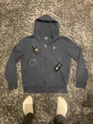 Mörkblå ziphoodie från Polo Ralph Lauren - Snygg mörkblå hoodie från Polo Ralph Lauren med klassisk logga broderad på bröstet. Tröjan har huva med snörning, dragkedja framtill och två fickor. Slim fit-modell i mjuk bomull som är perfekt för chill dagar. Passar dig som gillar stilren och enkel design.                                  Sorleken är en slimmad M.                                          Pris kan diskuteras!