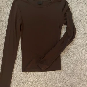 Brun långärmad topp från Gina Tricot - Snygg brun långärmad topp från Gina Tricot. Perfekt för lager-på-lager eller att bära som den är. Enkel och stilren design som passar till många olika outfits.