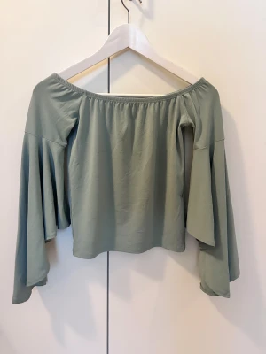 Grön offshoulder topp med vida ärmar - Snygg ljusgrön offshoulder topp med långa, vida ärmar. Toppen har en mjuk och flowy passform som ger en chill vibe. Perfekt att styla med jeans eller kjol för en cool look. Materialet känns lent och lätt mot huden.