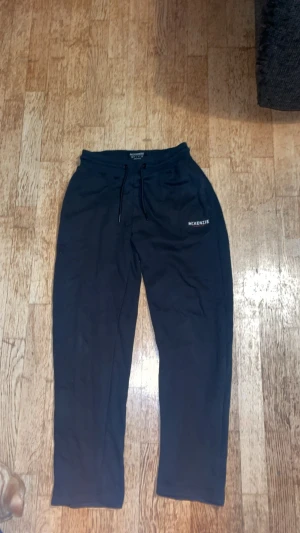 Svarta mjukisbyxor från McKenzie - Svarta mjukisbyxor från McKenzie med snörning i midjan och logga på vänster sida. Sköna och avslappnade med normal passform, perfekta för chill eller träning. Tillverkade i mjukt bomullsmaterial för extra komfort.