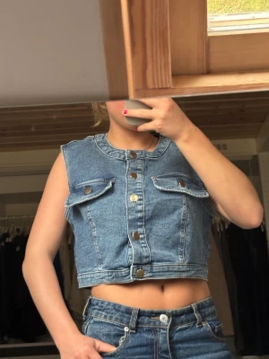 Jeansväst - INTRESSEKOLL!!! Snygg croppad jeansväst från H&M i klassisk blå denim. Västen har rundad krage, tryckknappar i silver och två bröstfickor med lock. Perfekt att styla över en t-shirt eller klänning för en cool look.  Nästan aldrig använd🫶🏽🫶🏽