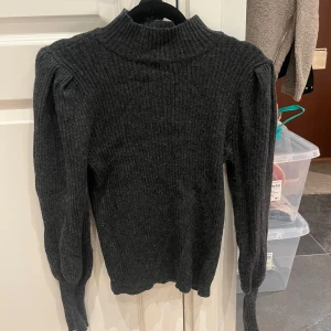 Mörkgrå ribbad polotröja från ONLY - Säljer en mörkgrå ribbstickad polotröja från ONLY i storlek S. Tröjan har lång ärm, hög krage och markerade axlar för en trendig look. Perfekt för lager-på-lager under kyliga dagar.