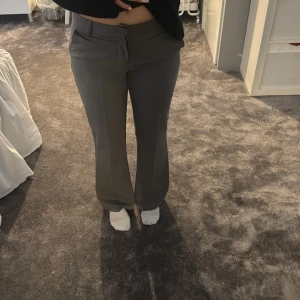 Grå kostymbyxor med bootcut - Snygga grå kostymbyxor med bootcut och normal passform. Byxorna har klassisk design med fickor fram och bälteshällor i midjan. Perfekta för en stilren look och passar till många olika outfits. Low waist