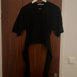 Svart croppad topp med knyt bak från lager 157 - Svart croppad topp från 157 med rund halsringning och korta ärmar. Toppen har långa band som hänger ner från sidorna, perfekt för att knyta eller låta hänga fritt för en edgy look. Enkel och stilren design som sticker ut.