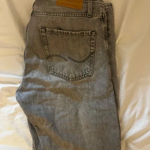 Grå loose fit jeans från Jack & Jones - Säljer ett par grå jeans från Jack & Jones i loose fit-modell. Jeansen har klassisk femficksdesign, raka ben och snyggt tvättad finish. Perfekta för dig som gillar en avslappnad och trendig look. Storlek 29/32.