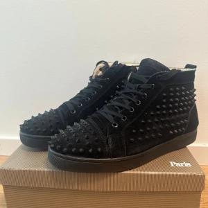 Christian Louboutin svarta sneakers med nitar - Svarta high-top sneakers från Christian Louboutin i mocka med svarta nitar över hela skon. Skorna har snörning, rund tå och svart platt sula. Insidan är ljus och mjukt vadderad för extra komfort. Riktigt edgy och sticker ut i mängden.