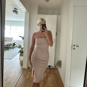 Blekrosa midiklänning med slits - Säljer en stilren blekrosa klänning med smala axelband och rak halsringning. Klänningen är figurnära och har en snygg slits framtill som ger extra edge. Materialet känns mjukt och har en lätt stretch. Perfekt för dig som gillar minimalistisk och clean stil.