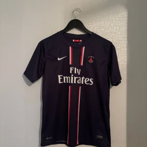 PSG fotbollströja 2012/13 - Säljer en officiell Paris Saint-Germain hemmatröja från säsongen 2012/13. Storlek: XL barn (passar XS/S herr), Märke: Nike Dri-FIT (orginal), Sponsor: Fly Emirates, Skick: Jättebra, inga defekter. En klassisk PSG-tröja i riktigt fint skick. Perfekt för samlare, fotbollsfans eller för att använda till match/träning. 