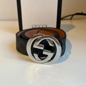 Svart bälte med silvrigt spänne - Säljer ett svart bälte i skinn med klassiskt mönster och ett stort, blankt. Bältet har en stilren och lyxig känsla, perfekt för att lyfta vilken outfit som helst. Med följer box och kvitto. Pris kan diskuteras vid snabb affär✅