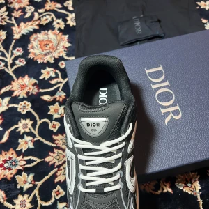 Dior B30 svarta sneakers - Säljer ett par Dior B30 sneakers i svart och vitt med coola reflekterande detaljer och tydlig Dior-logga på sidan. Skorna har mesh och syntetmaterial, vita snören och en chunky vit sula som ger en modern vibe. Perfekta för dig som vill sticka ut med lyxig streetstyle. Storlek på skorna är 42,5 men passande både för 42 och 43.