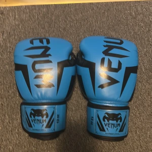 Venum handskar  - Säljer ett par blå boxningshandskar från Venum med svarta detaljer och logga. Handskarna är i storlek 12 oz och har en klassisk form med bred kardborrestängning runt handleden. Perfekta för träning och sparring. Snygg design som sticker ut på gymmet.