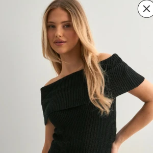 Svart ribbad offshoulder stickad topp - Säljer en svart stickad topp med ribbad struktur och offshoulder-modell. Toppen har korta ärmar och en bred, vikt kant över axlarna som ger en snygg och trendig look. Perfekt att styla med både jeans och kjol.