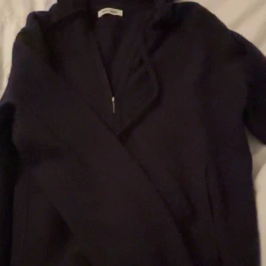 Mörkblå zip hoodie i kashmir från Soft Goat - Mörkblå hoodie från Soft Goat i lyxig kashmir. Tröjan har dragkedja framtill, huva med snörning och två fickor. Den är långärmad och har en normal passform, perfekt för en chill och stilren look. Storlek M men passar även S