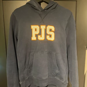 Mörkblå hoodie från Parajumpers - Snygg mörkblå hoodie från Parajumpers med stor PJS-logga i gult och vitt framtill. Klassisk känguruficka, huva och broderad patch på ärmen. Perfekt för dig som gillar streetwear och vill ha en stilren men sportig look.