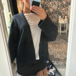 Svart stickad kofta med loose fit - Mysig svart stickad kofta med öppen front och breda ärmar. Koftan har en loose passform och är perfekt att slänga över en t-shirt. Enkel och stilren design som funkar till många outfits.