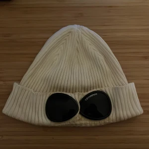 Vit ribbad mössa C.P. Company - Cp company mössa, riktigt skön på vintern och snygg. Lite lite repig på glaset bara men annars väldigt bra skick!