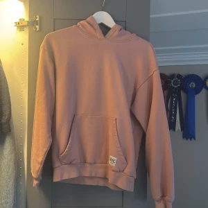 Ljusrosa hoodie från H&M NYC - Ljusrosa hoodie från H&M med NYC-märke vid fickan. Tröjan har huva, magficka och ribbade muddar vid ärmslut och nederkant. Mjuk insida i fleece och avslappnad passform, perfekt för chill dagar.